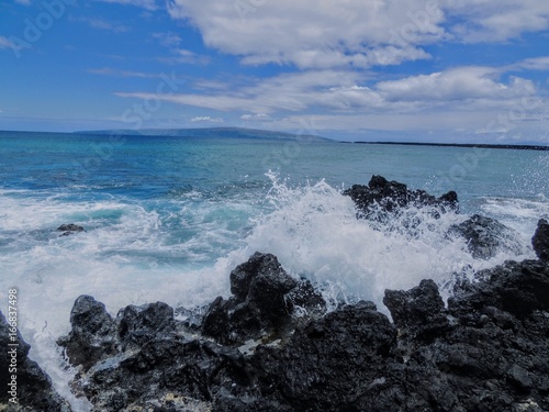 Lava Rock and Coral with Spray of crashing waves in beach tide pools at Maluaka Beach and Kihei Maui with sky and clouds
