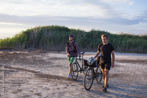 Two tourists with bicycle walking in the desert during the sunset in lake 