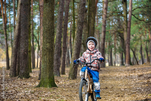 Happy kid boy of 3 or 5 years having fun in autumn forest with a bicycle on beautiful fall day. Active child wearing bike helmet. Safety, sports, leisure with kids concept.