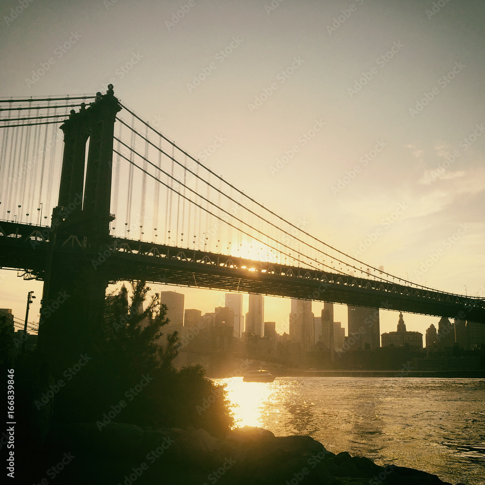 Warm light, sunset over Manhattan skyline. View of the Manhattan Bridge from Brooklyn Bridge Park looking towards Manhattan's financial district at sunset. Manhattan Bridge spanning the East River. Warm light, sunset over Manhattan skyline. View of the Manhattan Bridge from Brooklyn Bridge Park looking towards Manhattan's financial district at sunset. Manhattan Bridge spanning the East River.