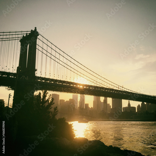 Warm light, sunset over Manhattan skyline. View of the Manhattan Bridge from Brooklyn Bridge Park looking towards Manhattan's financial district at sunset. Manhattan Bridge spanning the East River.