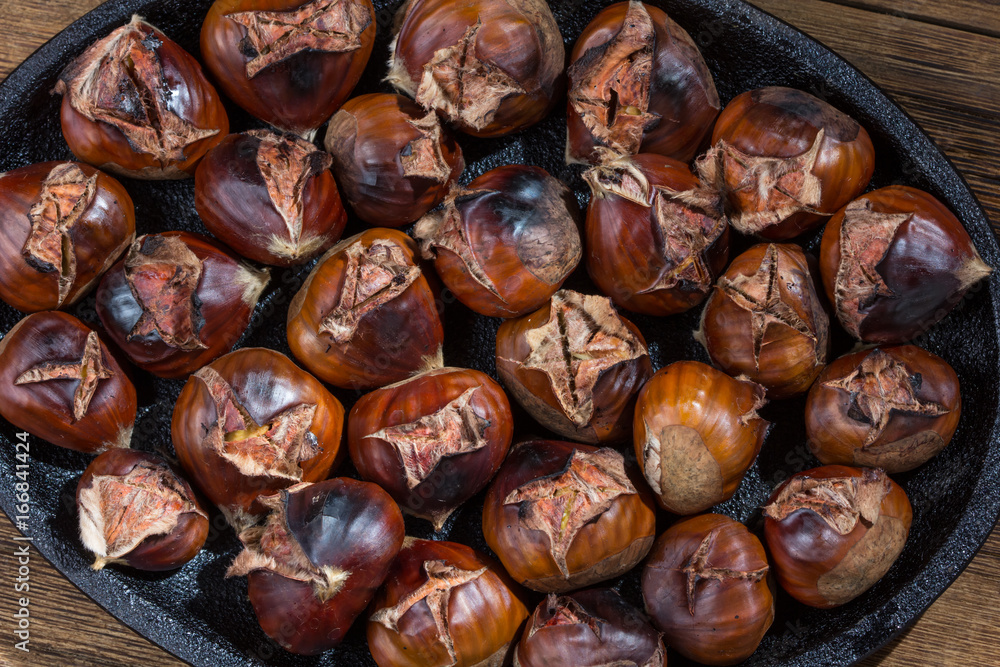 Roasted sweet chestnuts on iron pan, rustic wooden table. Autumn background. Top view Roasted sweet chestnuts on iron pan, rustic wooden table. Autumn background. Top view