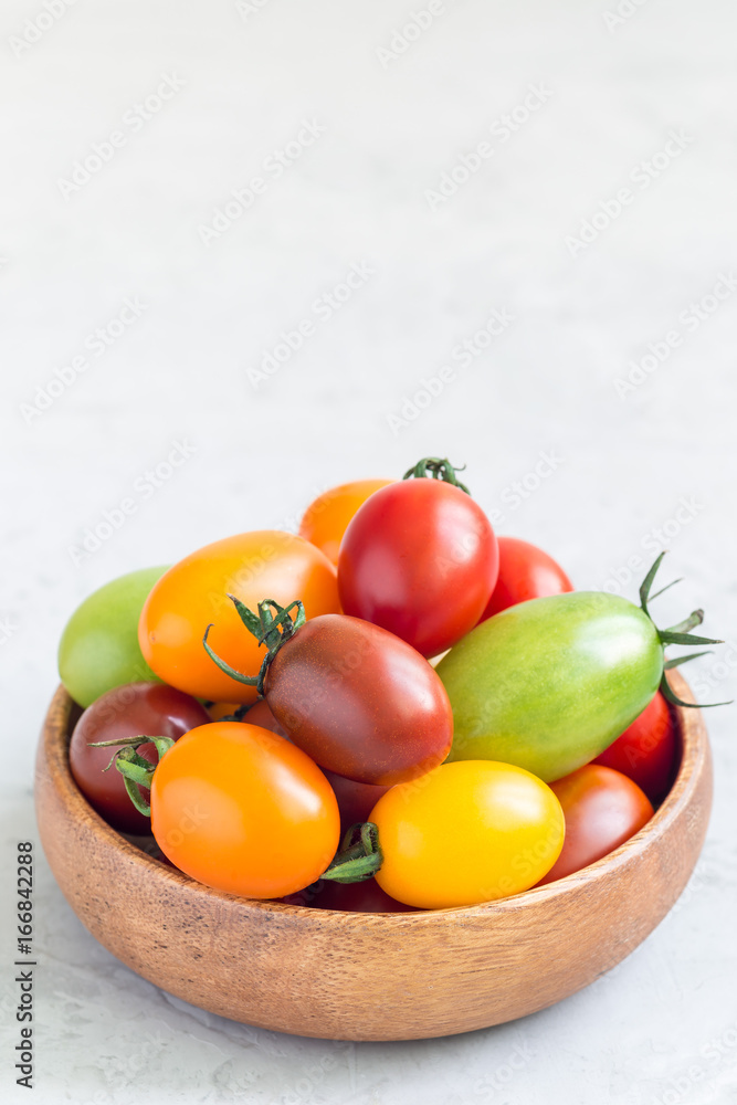 Small colorful cherry tomatoes in wooden bowl on table, vertical, copy space