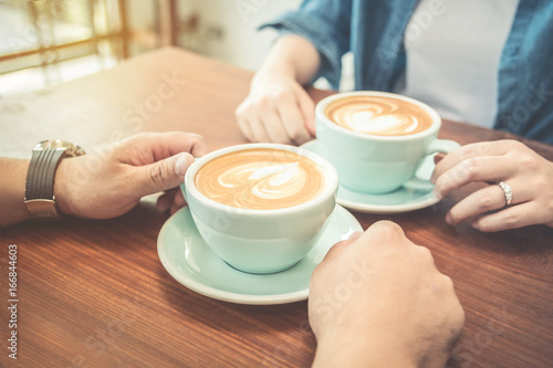 hands of couple drinking coffee at cafe together  heart shape latte art in coffee cup.