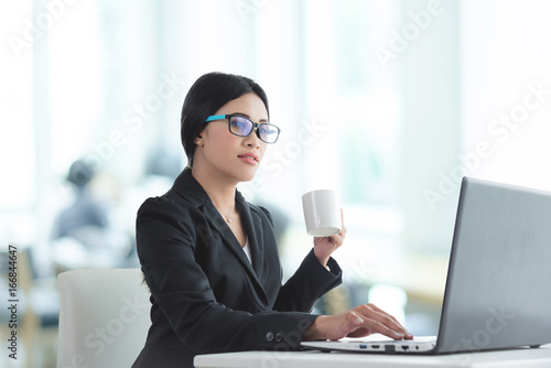 Beautiful asian businesswoman in black suit sitting and working with notebook computer in office