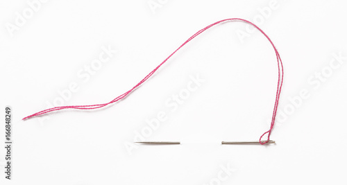 Sewing needle with red thread through the white background