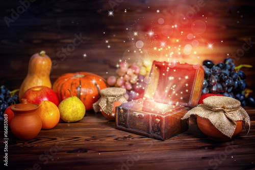 Fototapeta Naklejka Na Ścianę i Meble -  thanksgiving concept of pumpkins, apple, garlic, straw and opened chest treasure with mystical miracle light on wooden table, beautiful fine art design