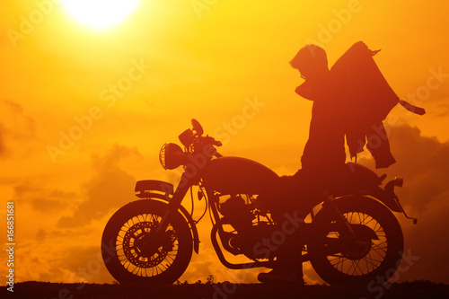 Silhouette of biker man with his motorbike beside the natural lake and beautiful, enjoying freedom and active lifestyle, having fun on a bikers tour.sunset background and sky.