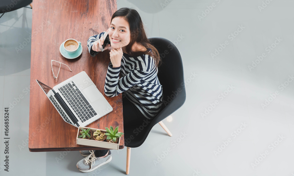 Young beautiful Asian woman working and talking with smart phone and laptop in coffee shop background with copy space.Concept of female freelancer.Vintage tone