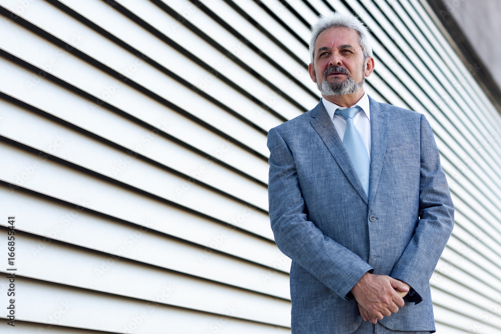 Senior businessman with arms crossed outside of modern office building.