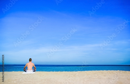 A man doing meditation or yoga on the beach on sunshine day © PixHound