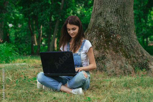 cutie young girl using a laptop and sits on a grass