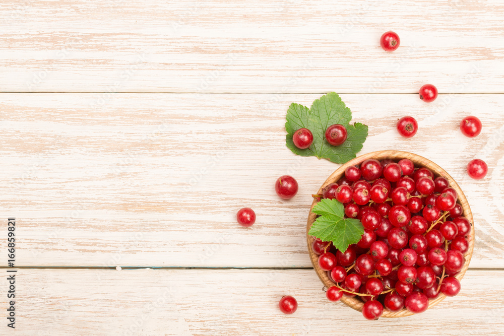 Red currant berries in a wooden bowl with leaf on the light wooden background with copy space for your text. Top view Red currant berries in a wooden bowl with leaf on the light wooden background with copy space for your text. Top view