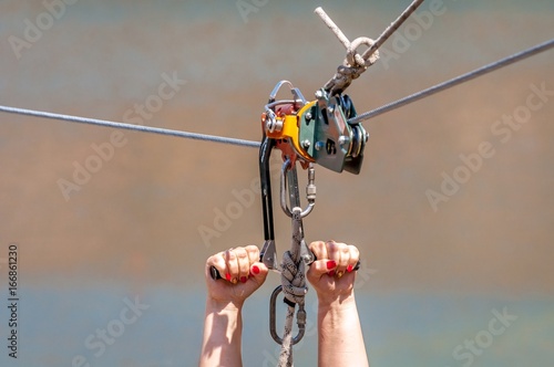 Zipline. Equipment for safe sliding on steel cable. Woman's hands close-up during the flight. photo