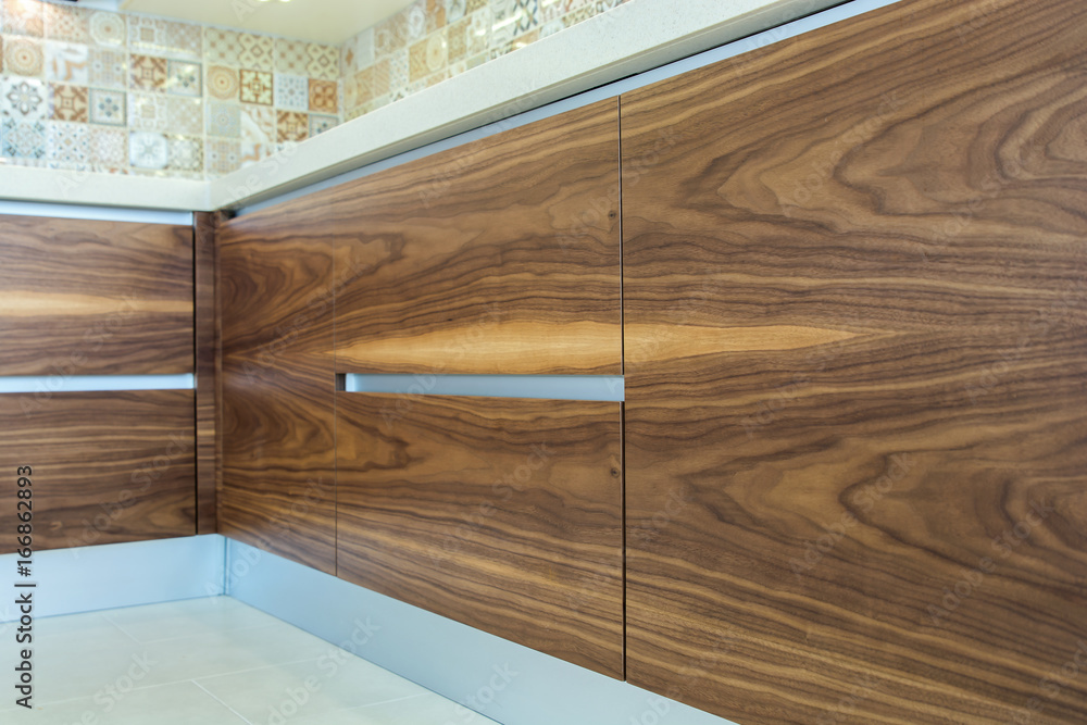 Fototapeta premium Modern home interior. Texture of the wood of the facades of the modern kitchen are made from walnut veneer. European furniture, design, technologies. Fine design. Refinishing kitchen cabinets. 