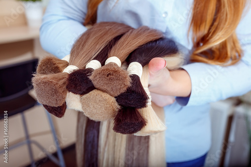 Woman holds hair extension equipment of natural hair. hair samples of different colors photo