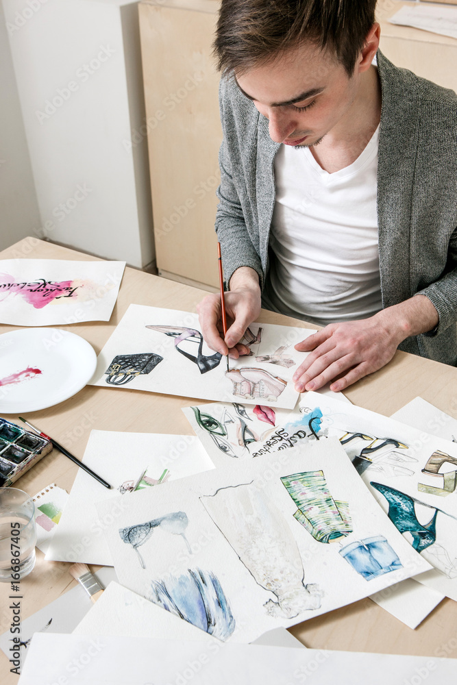 Designer of fashion indusrty works on sketches footwear model on workplace with artistic tools around Designer of fashion indusrty works on sketches footwear model on workplace with artistic tools around