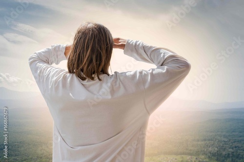 Looks into the distance.
A man of mature years in white clothes looking from the mountain to the horizon with his hands up to his eyes.Morning