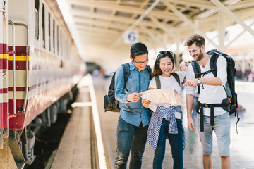 Multiethnic group of friends, backpack travelers, or college students using local map navigation together at train station platform. Asia travel destination, tourism activity, or railroad trip concept