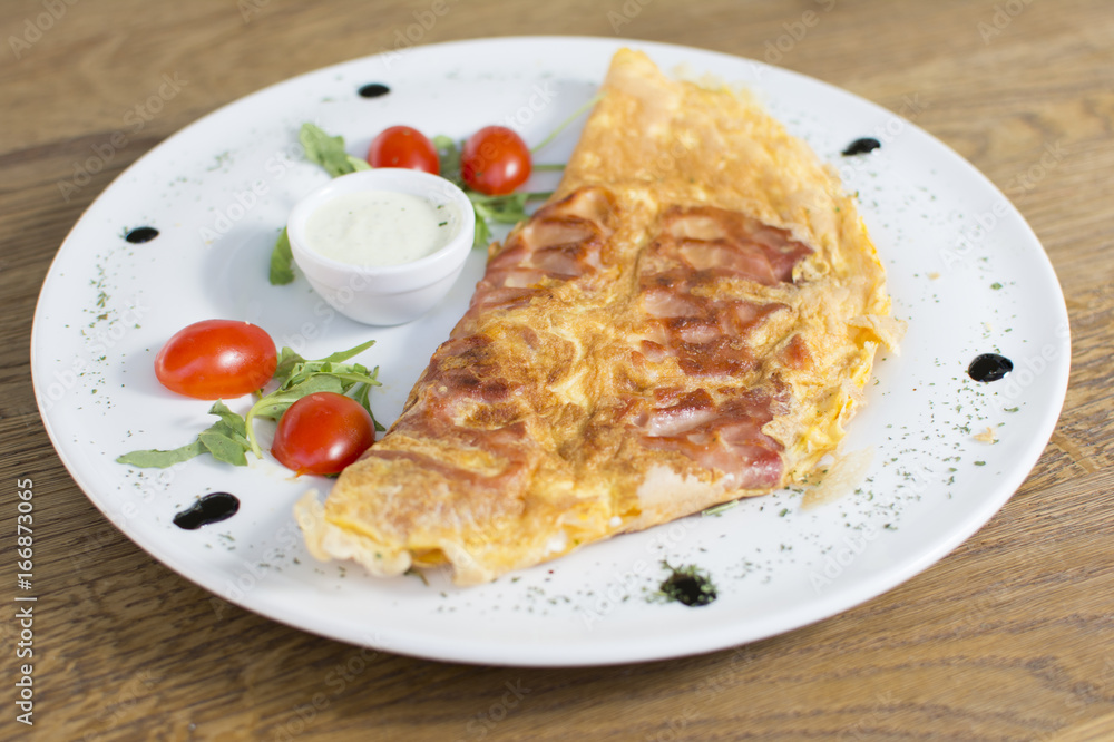 Scrambled eggs with ham on a plate on the wooden table. Tomato and sour cream on the side. Scrambled eggs with ham on a plate on the wooden table. Tomato and sour cream on the side.
