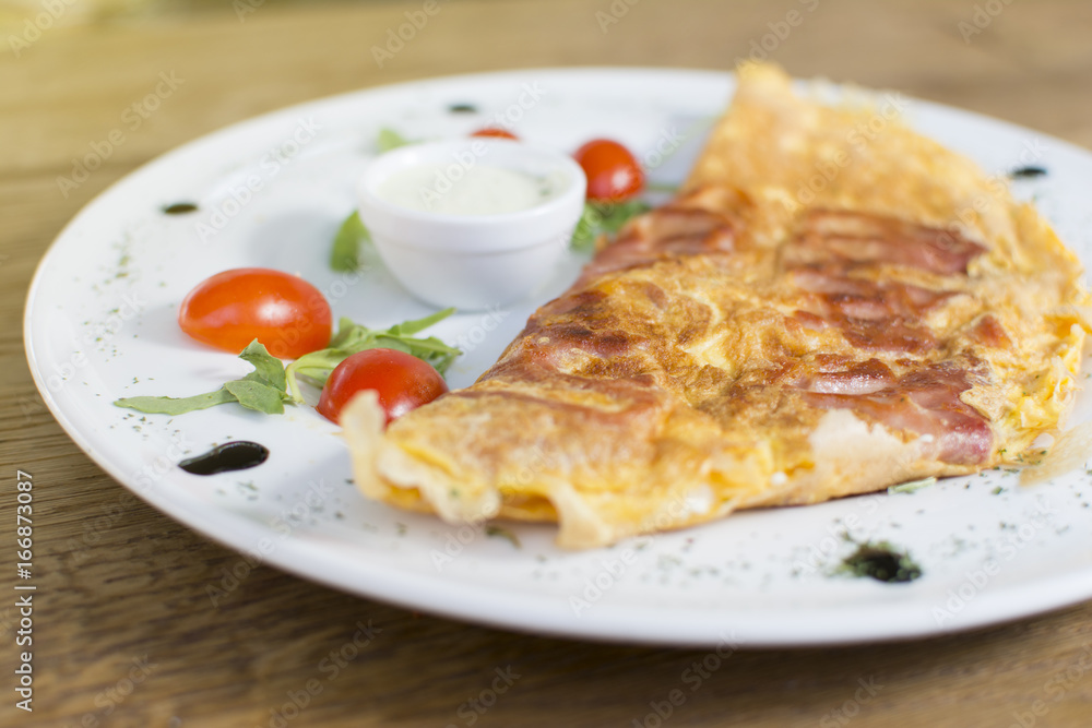 Scrambled eggs with ham on a plate on the wooden table. Tomato and sour cream on the side. Scrambled eggs with ham on a plate on the wooden table. Tomato and sour cream on the side.