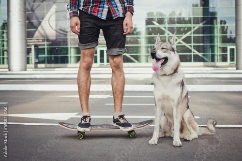 Close up of man on skateboard with siberian husky dog on street road