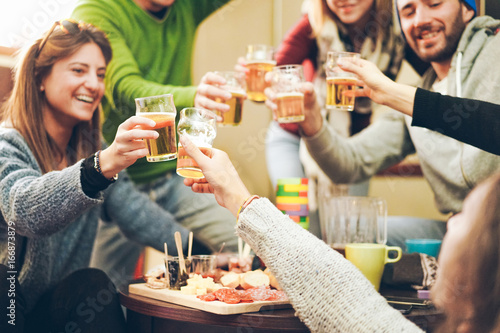 Group of happy friends cheering with beer after skiing day in bar pub restaurant - Young people toasting appetizer in brewery chalet - Concept about good and positive mood - Focus on right bottom hand photo