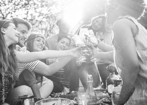 Happy friends cheering with wine glasses at pic-nic lunch outdoor - Young students having fun doing a toast and eating in nature - Food and youth concept - Focus on right bottom hand - Vintage filter