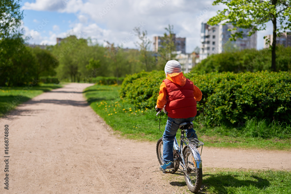 Fototapeta premium Small boy ride bicycle in street park. He is pointing moving dow
