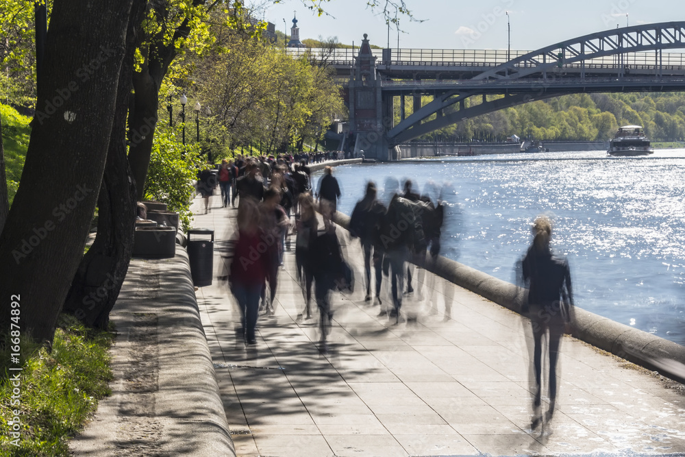 silhouettes of people walk along the embankment of a city river