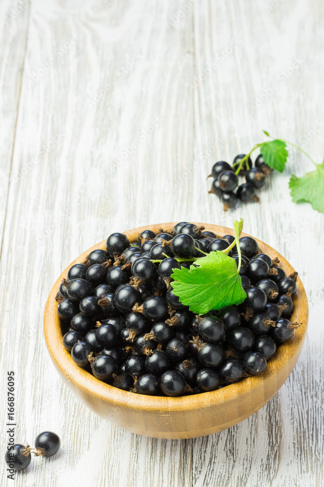 Black currant in a wooden bowl on white shabby wooden table. Summer snack, dessert. Black currant in a wooden bowl on white shabby wooden table. Summer snack, dessert.
