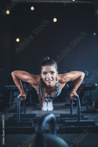 Beautiful young fit woman stretching and posing in fitness gym. Low light scene.