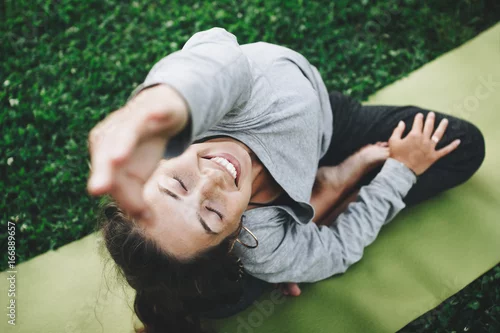 Fototapeta na wymiar Rozochocona i szczęście młoda kobieta ćwiczy joga na zielonym gazonie outdoors. Spokój i relaks, kobiece szczęście
