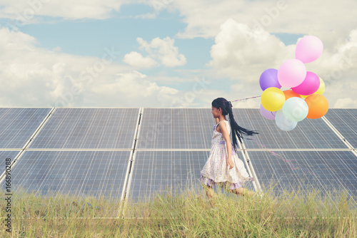 A funny girl carrying a colorful balloon running in a meadow with a Solar panel, photovoltaic. Concept of Eco-Friendly ,Clean Energy , Pure energy and Sustainable energy