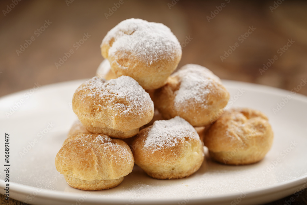 closeup shot of profiteroles covered with sugar powder on white plate on wooden table