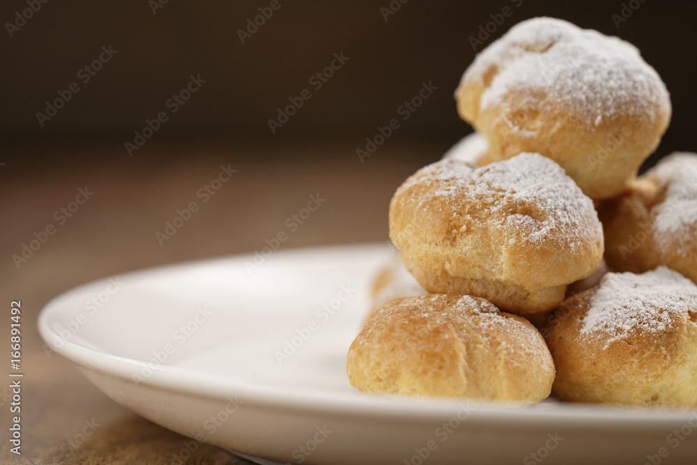 closeup shot of profiteroles covered with sugar powder on white plate on wooden table closeup shot of profiteroles covered with sugar powder on white plate on wooden table