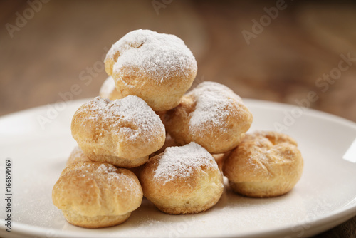 closeup shot of profiteroles covered with sugar powder on white plate on wooden table