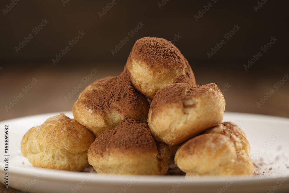 closeup shot of profiteroles covered with cocoa powder on white plate on wooden table