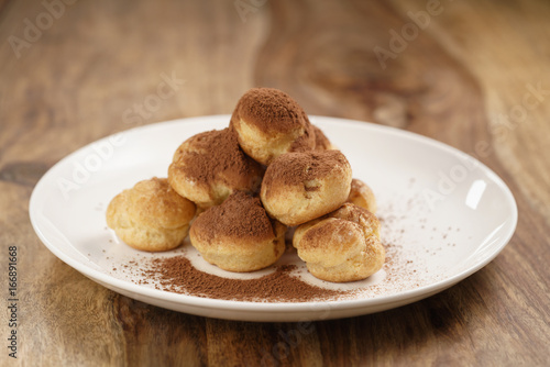 profiteroles covered with cocoa powder on white plate on wooden table