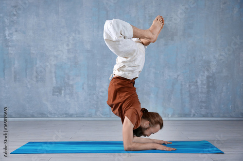 Young man practicing yoga on gray wall background