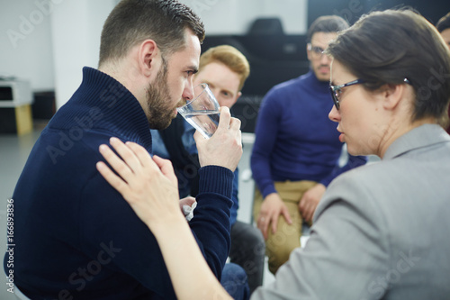 Helpful woman reassuring her co-worker with glass of water among other colleagues