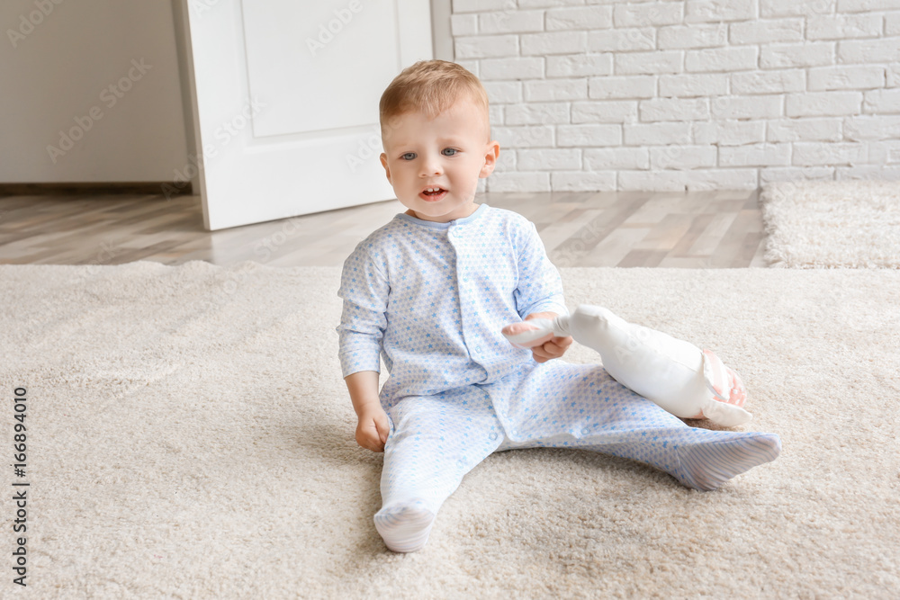 Cute baby boy sitting on carpet and playing with toy near wet spot Cute baby boy sitting on carpet and playing with toy near wet spot