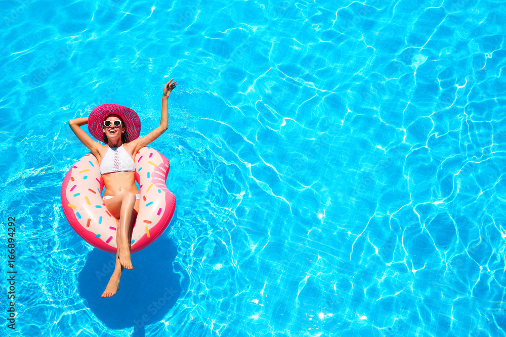 Naklejka premium Beautiful young woman relaxing on inflatable donut in blue swimming pool