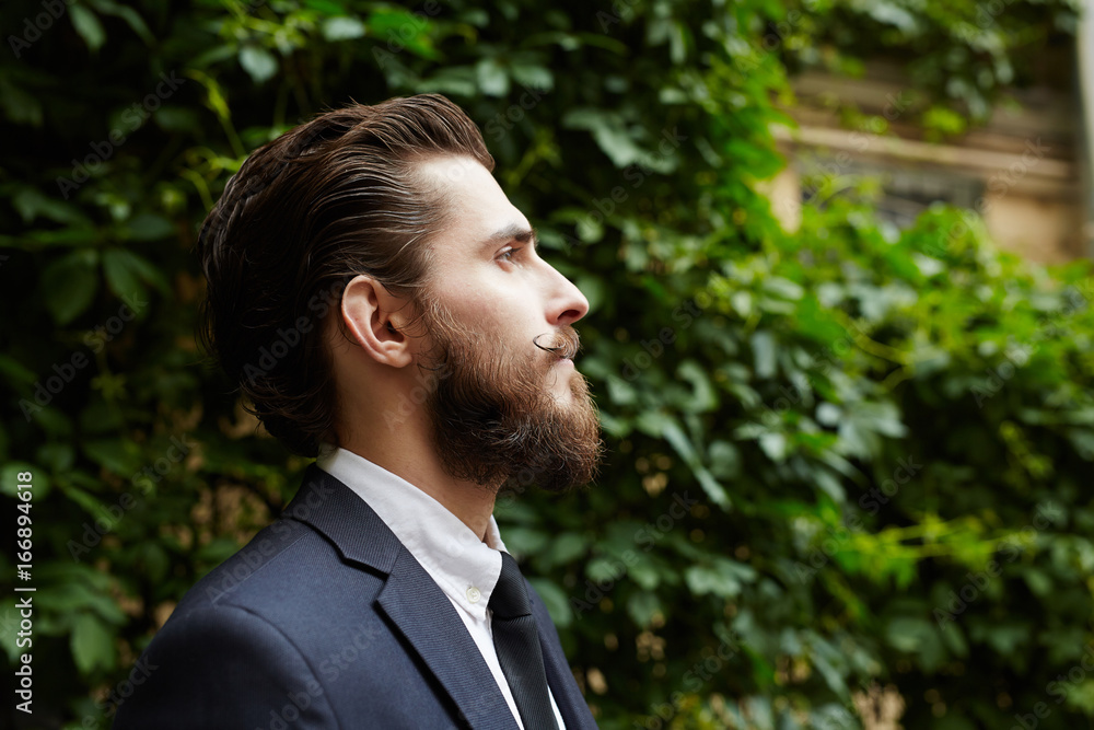Profile of groomed man in suit against green foliage Profile of groomed man in suit against green foliage