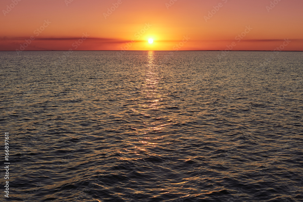 Deep sunset over calm smooth sea with bright colors and plenty of copy space. Beautiful natural summer seascape. Image of sunset with yellow red gradient colors. Horizontal photo. Red purple sunset
