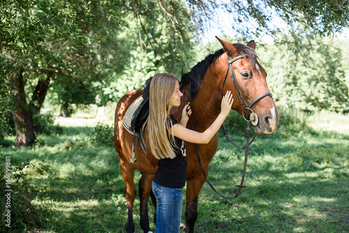 The girl takes care and stroke a horse in a green garden. Love for animals