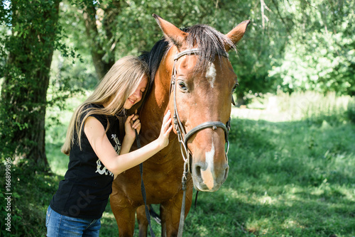 The girl takes care and stroke a horse in a green garden. Love for animals