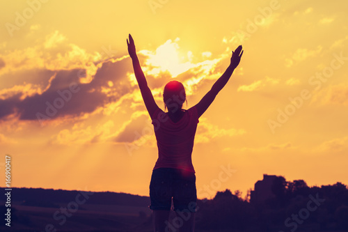 Silhouette of a young woman with arms raised in the backdrop of the setting sun