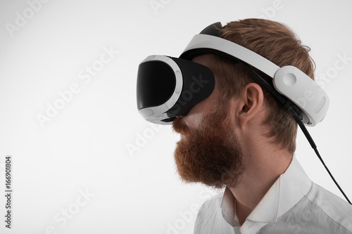 Futuristic technology, gaming, cyberspace and innovations concept. Handsome young Caucasian businessman with thick beard wearing 3d oculus rift headset, experiencing virtual reality in his office