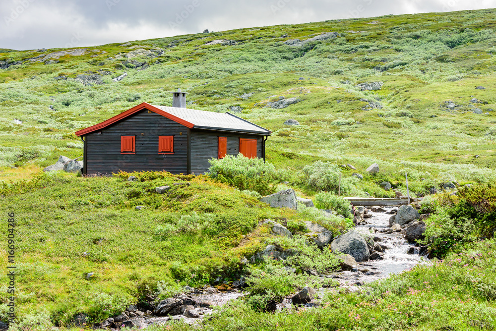 Mountain landscape with black and red cabin beside small stream. Location Hardangervidda in Norway. Mountain landscape with black and red cabin beside small stream. Location Hardangervidda in Norway.